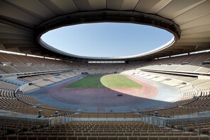 Un estadio interior con asientos escalonados, una pista central y una gran estructura suspendida.