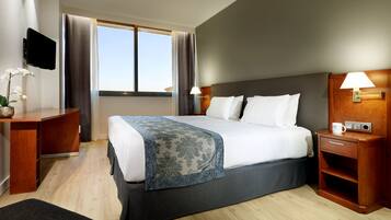 Una habitación de hotel con cama, mesitas de noche, televisor y ventana con cortinas.