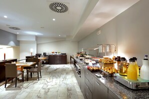 Un comedor de hotel moderno con suelo de mármol, un bufé con diversas opciones de comida y un área de estar con mesas y sillas.