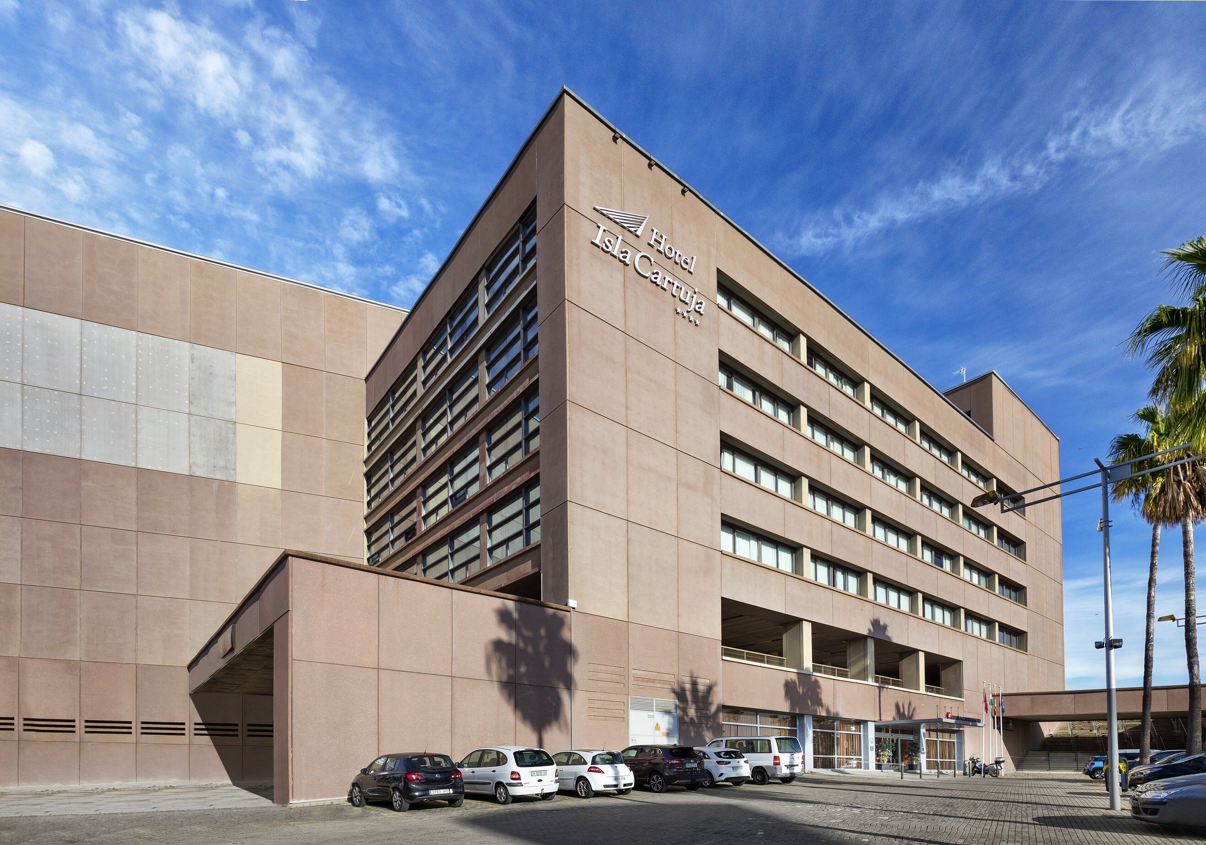 A modern hotel building with a prominent sign, multiple parking spaces, and a clear sky.