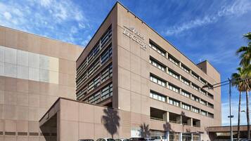 A modern hotel building with a prominent sign, multiple parking spaces, and a clear sky.