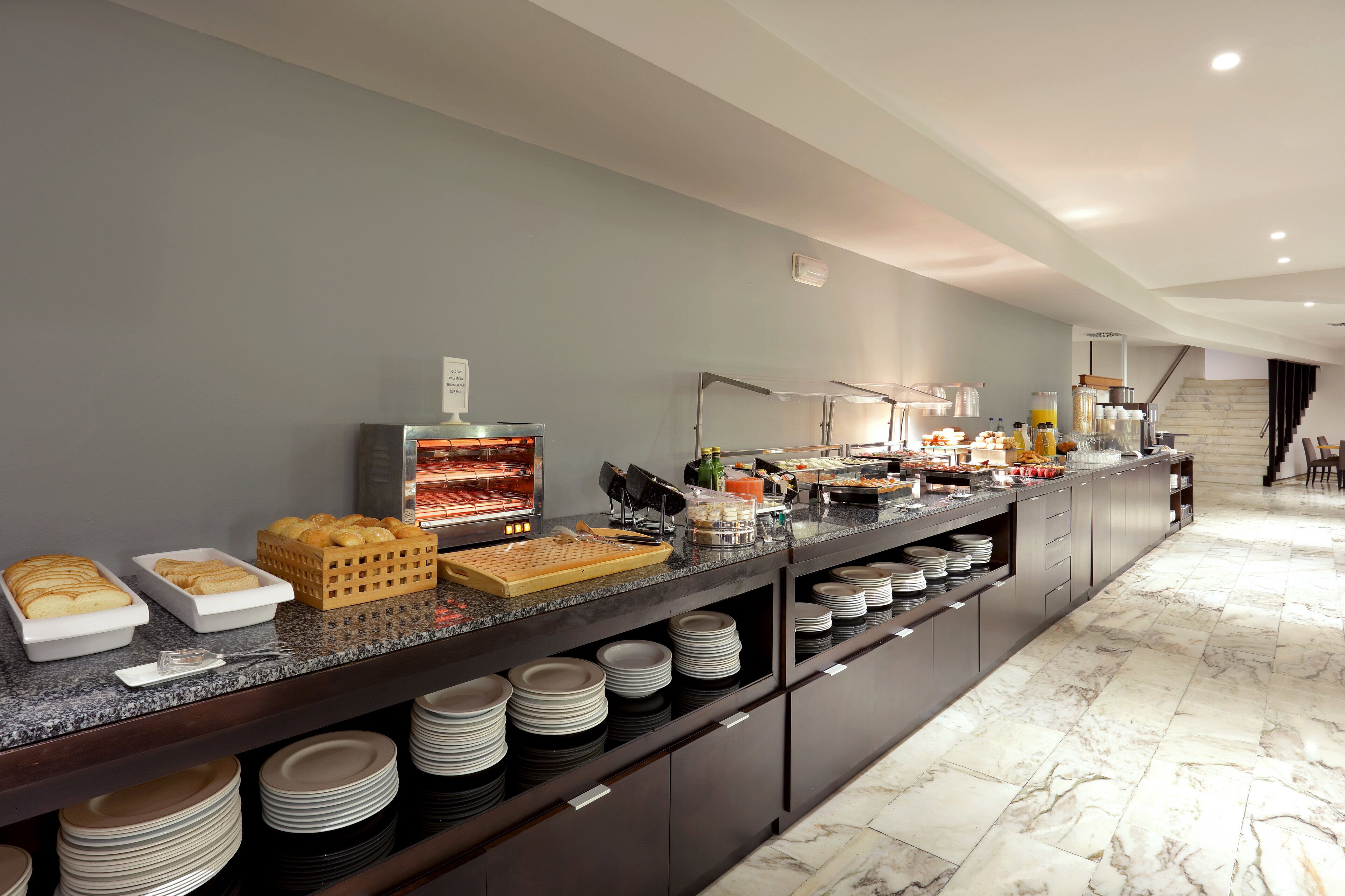 Disposició de buffet amb diferents plats i begudes, un sòl de marbre i una escala al fons.