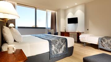 A hotel room with a large bed, a smaller bed, a desk, a TV, and a window with curtains.