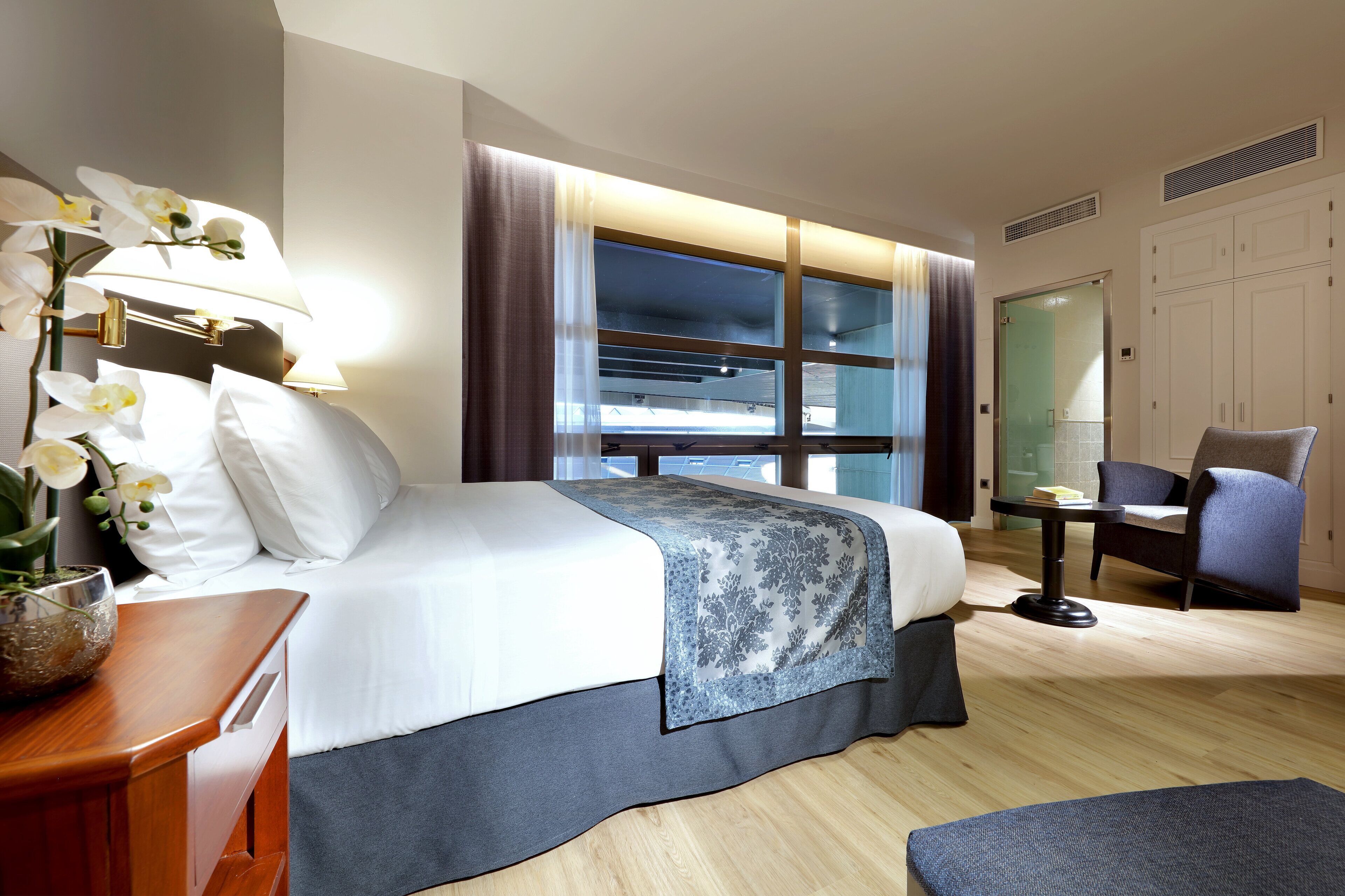 A hotel room with a bed, a chair, a table, and a window with curtains.