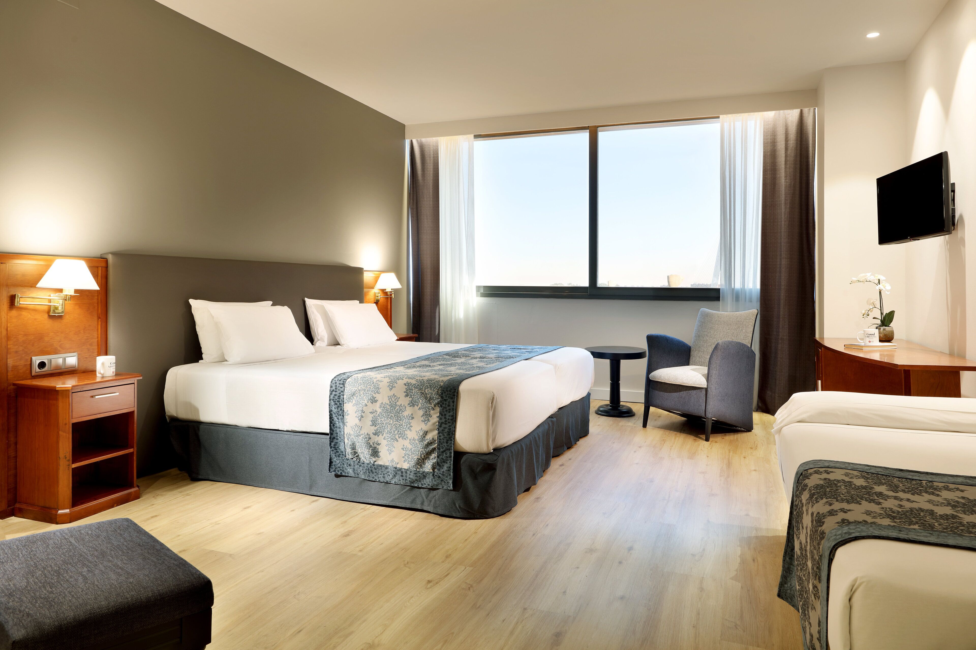 Ein Hotelzimmer mit Bett, Nachttischen, Schreibtisch, Stuhl und Fernseher.