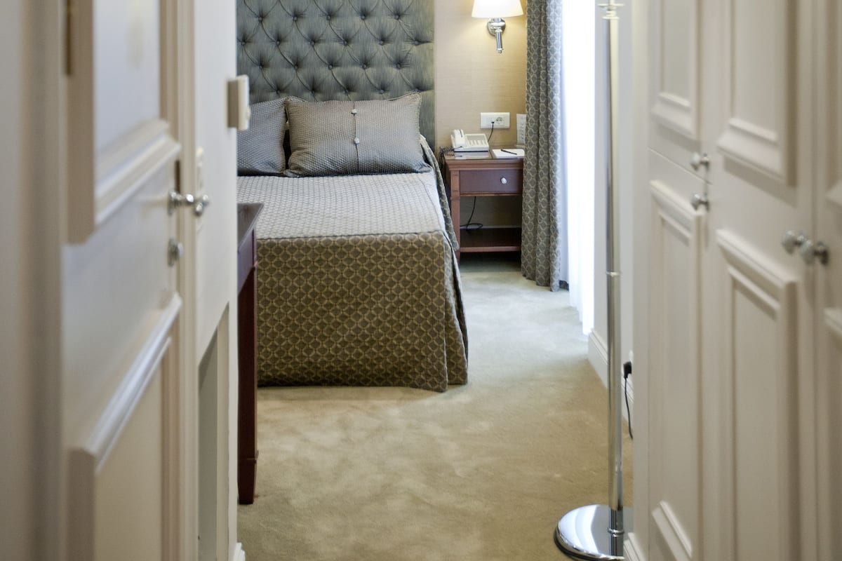 Habitación de hotel con cabecera capitonada, lámpara de noche, teléfono y suelo alfombrado.