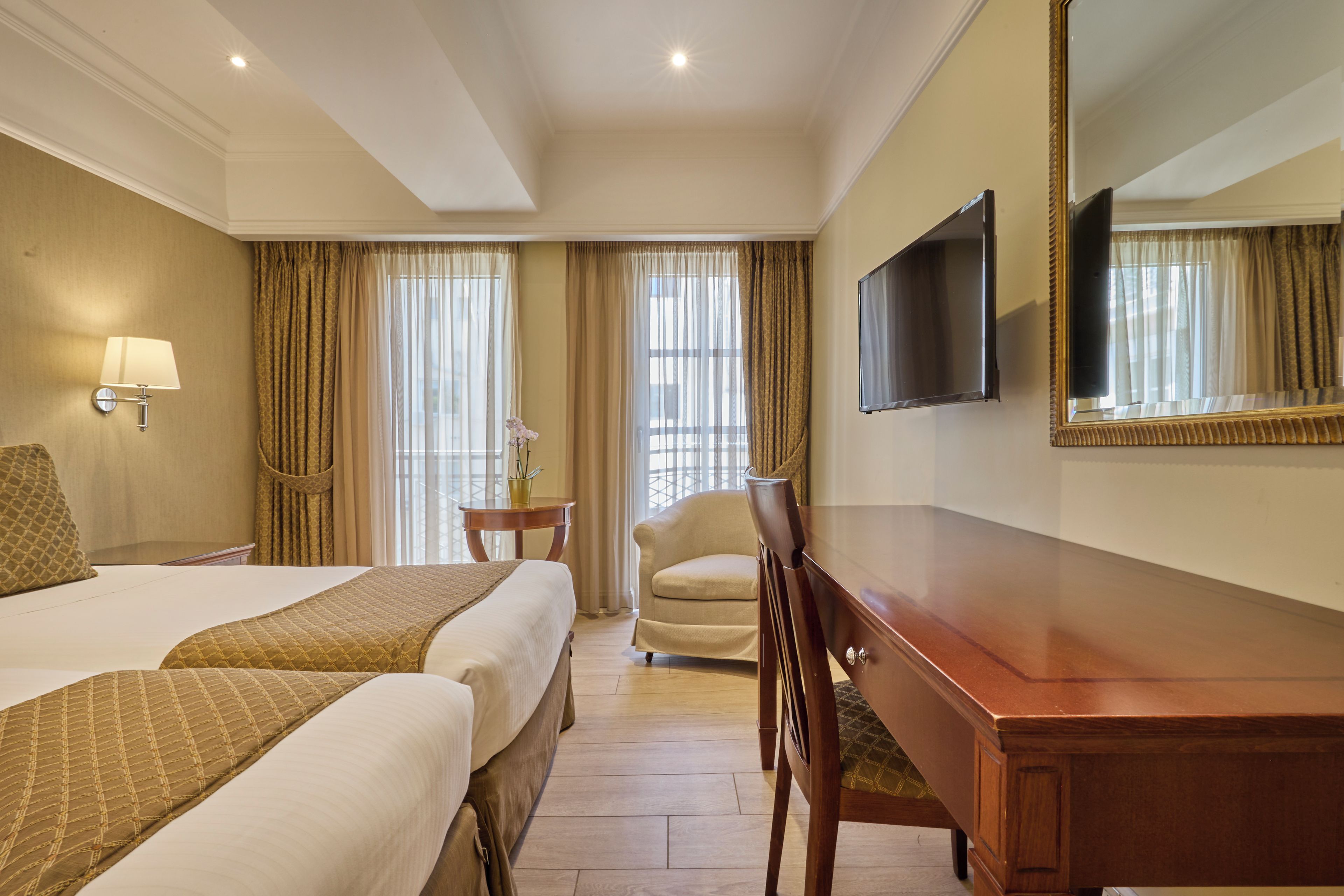A hotel room with a large bed, a desk, a chair, a television, and a window with curtains.