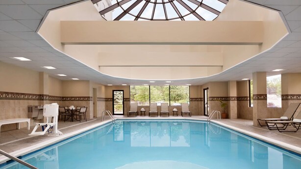 Una amplia piscina interior con tragaluces, sillones de descanso y un área de estar con mesas.