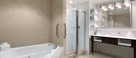 A modern bathroom with a large bathtub, a glass shower enclosure, and a vanity with a mirror and lights.