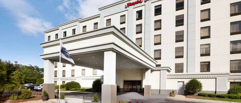 A hotel with a large entrance, a flag, and a small pond in front.