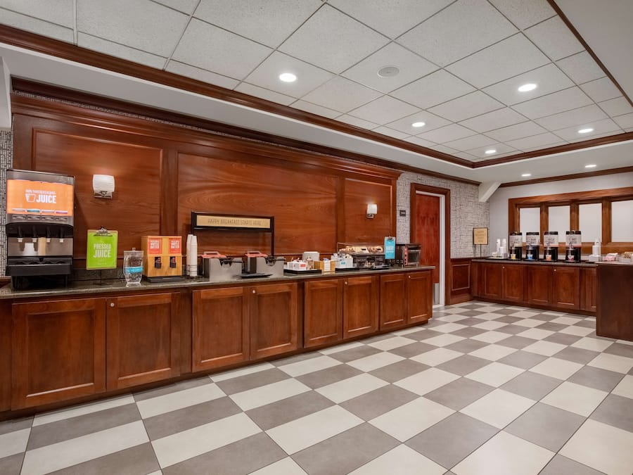 A hotel reception area with a checkered floor, wooden reception desk, and a coffee station.