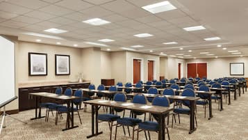 A conference room with rows of tables and chairs, a whiteboard, and framed pictures on the walls.