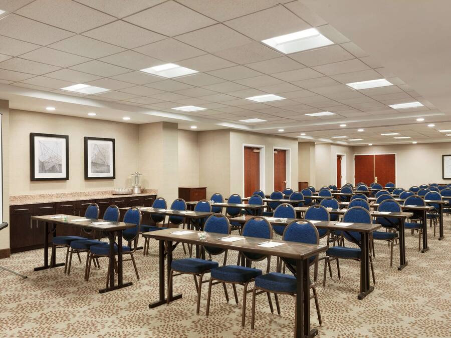 A conference room with rows of tables and chairs, a whiteboard, and framed pictures on the walls.