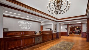 Zona de recepción de hotel con un mostrador de madera, un candelabro y un cartel de bienvenida.