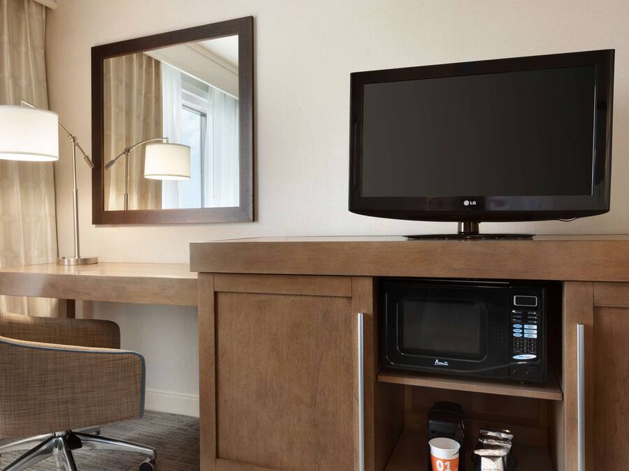 Habitación de hotel con escritorio de madera, televisión, microondas y una silla.
