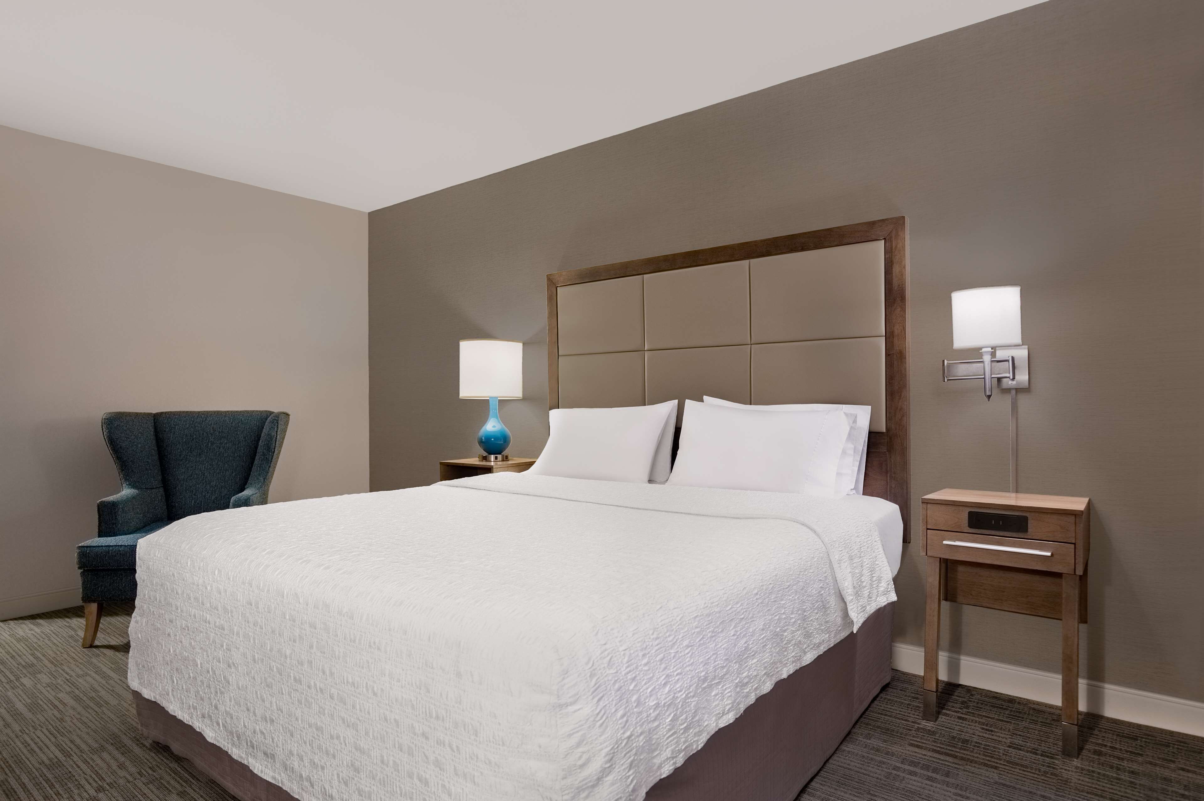 A hotel room with a large bed, two bedside tables, a chair, and a lamp.