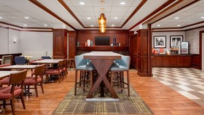 Comedor de hotel con mesas y sillas de madera, barra central y una pantalla de televisión.