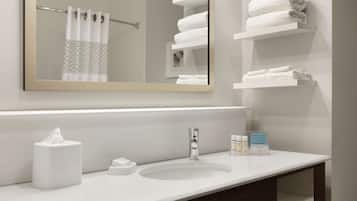 A bathroom with a white sink, a mirror, a towel rack, and a shelf with folded towels.