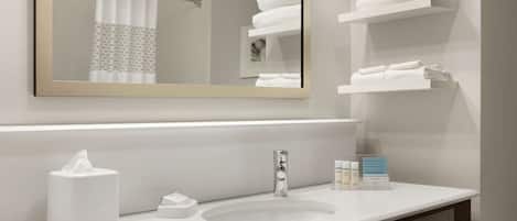 A bathroom with a white sink, a mirror, a towel rack, and a shelf with folded towels.