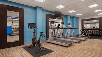 Un gimnasio con cintas de correr, elípticas y un espejo grande.