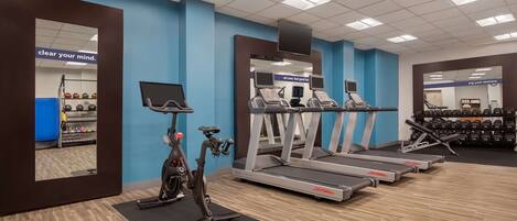 Een sportschool met loopbanden, een crosstrainer en een spiegelwand.