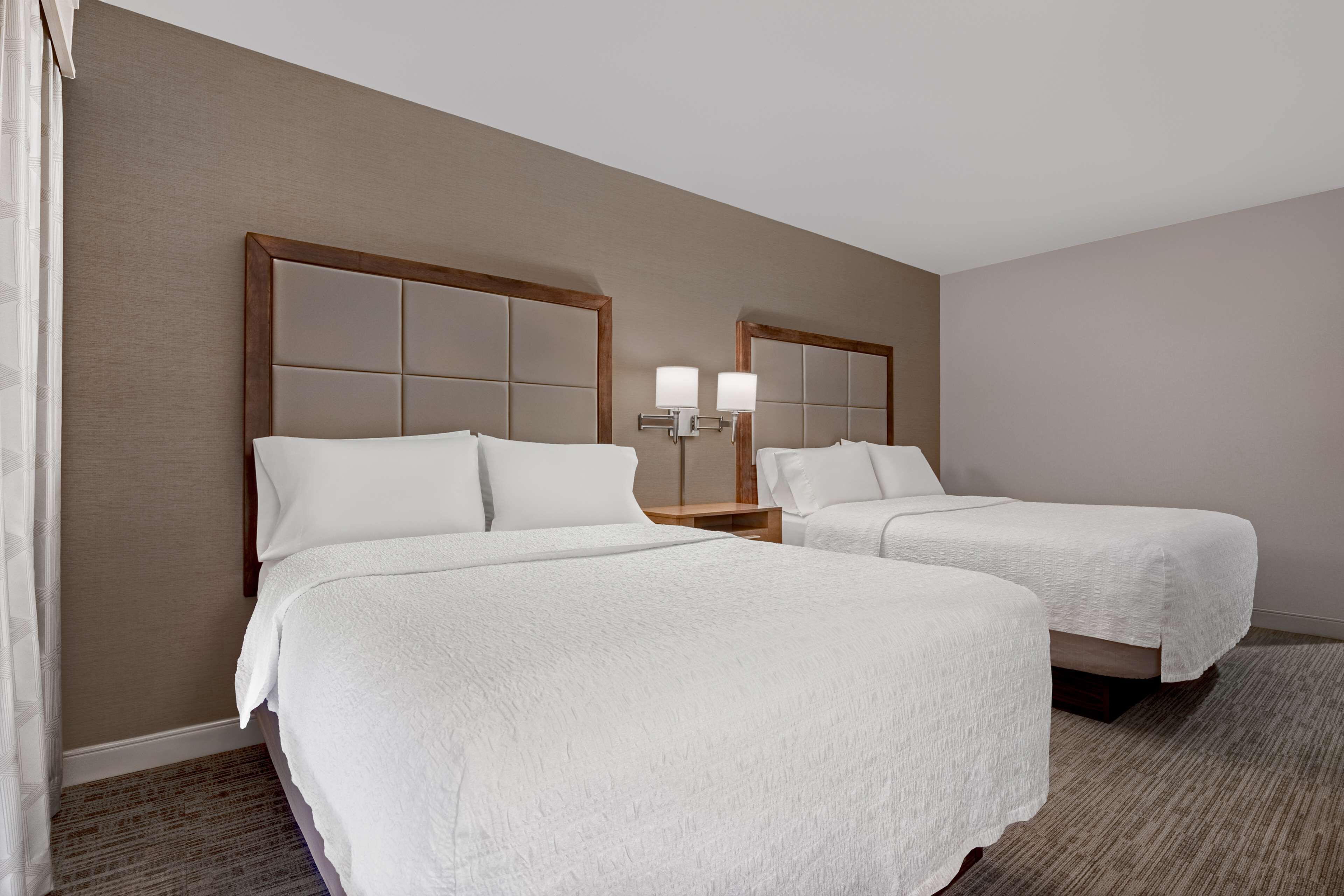A hotel room with two beds, a nightstand with a lamp, and a carpeted floor.