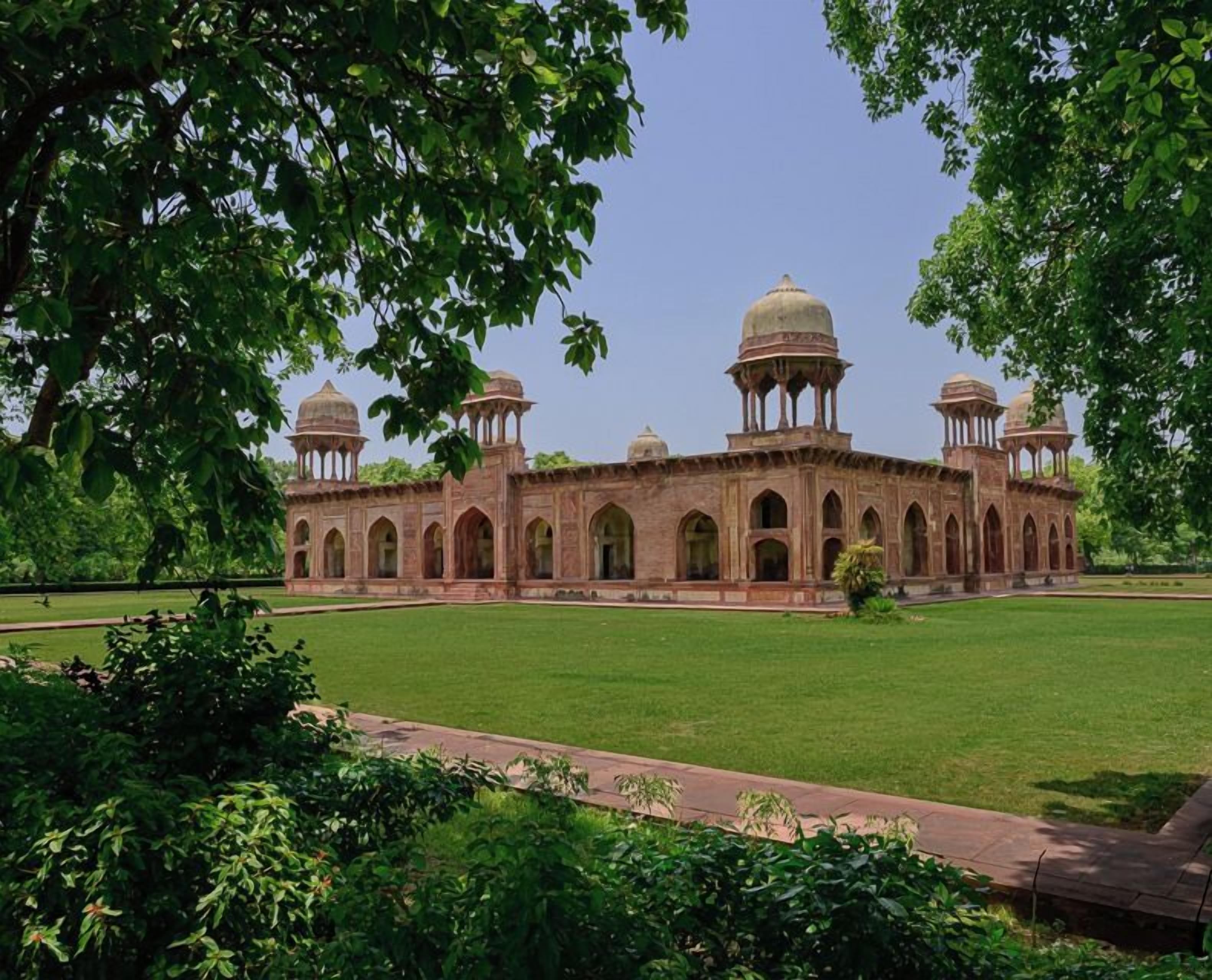 A large, historic building with multiple domes and arched windows, surrounded by a well-maintained lawn.