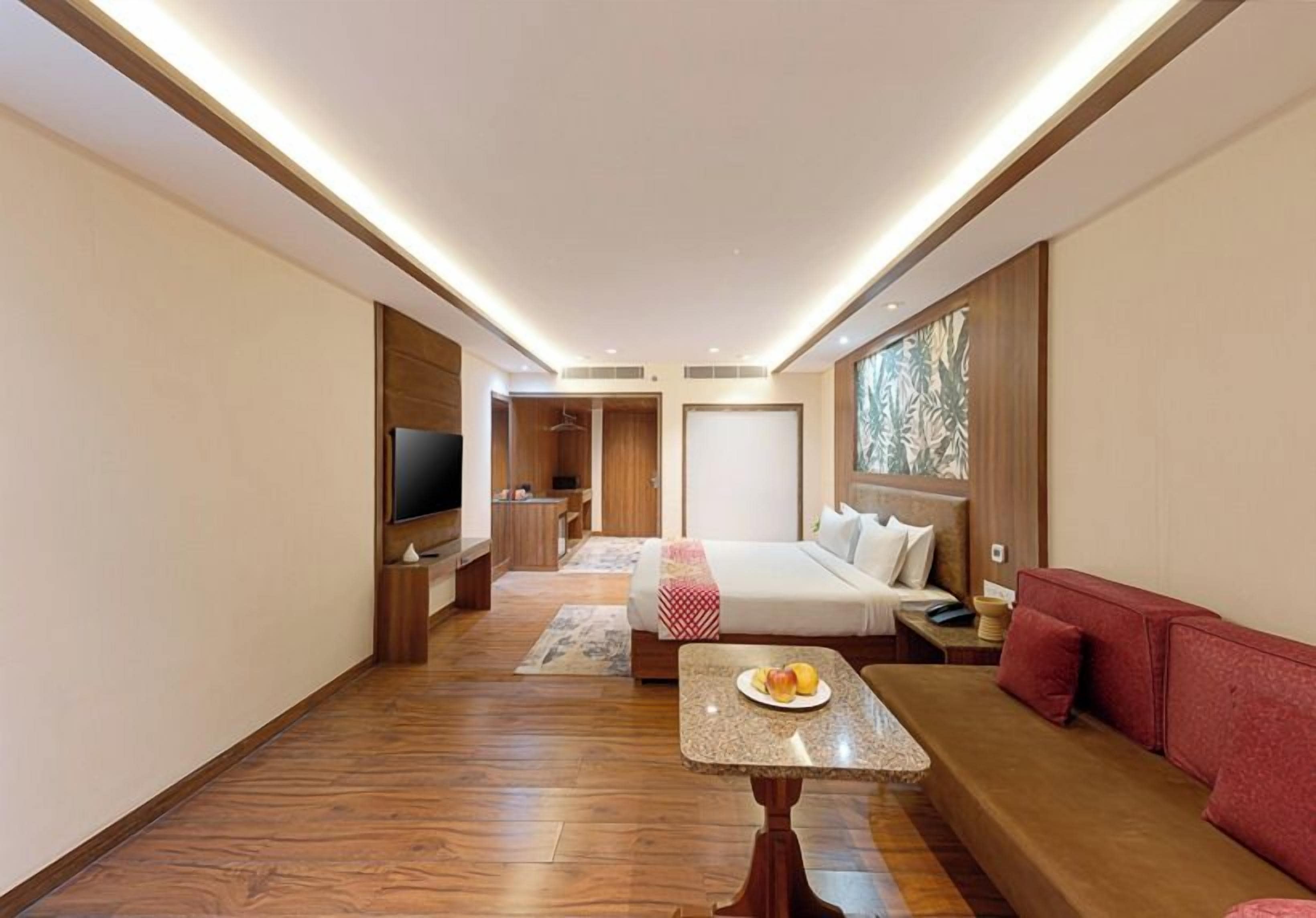 Habitación de hotel moderna con una cama, un televisor, una mesita con un plato de fruta y un sofá rojo.