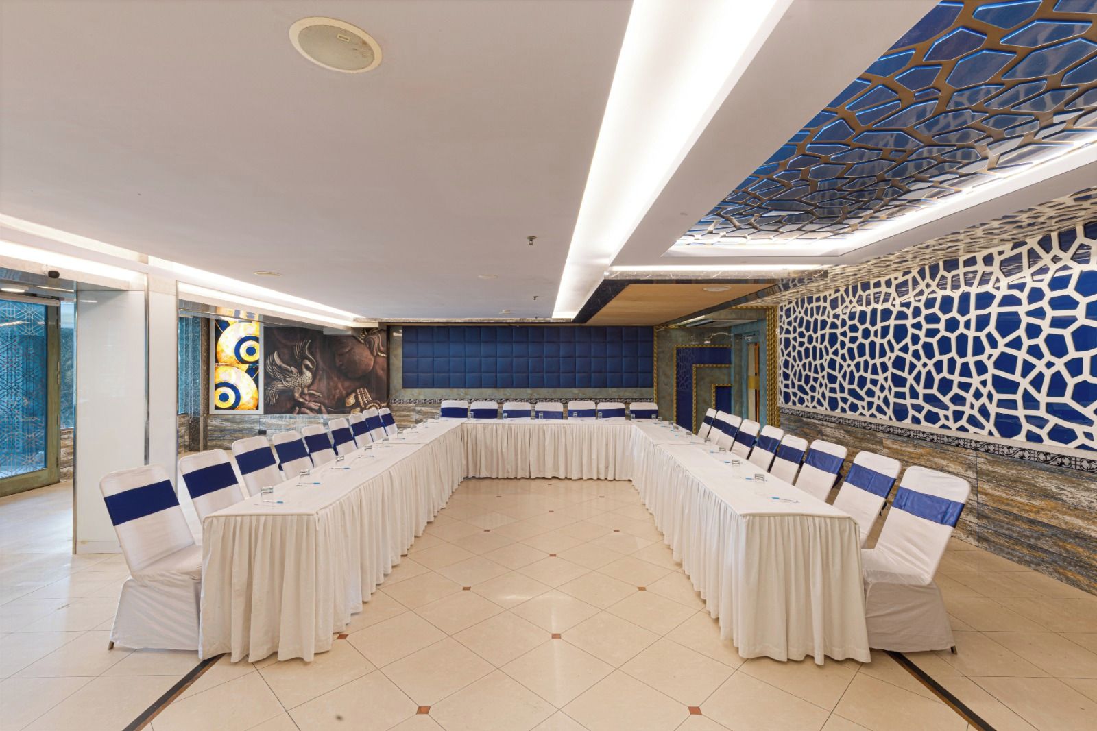 Una sala de conferencias con una larga mesa, sillas blancas y una pared con diseño azul.