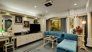 A well-appointed living room with a sofa, a television, a desk with a chair, and a coffee table. - Hotel Amar (Agra)