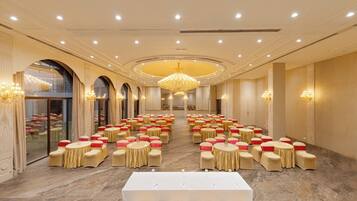 A banquet hall with round tables and chairs, a large chandelier, and a long table at the front.