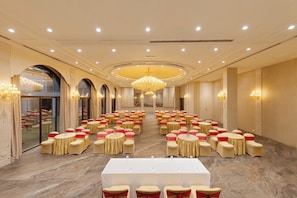 Un salón de banquetes con mesas y sillas redondas, una lámpara de araña grande y una mesa larga al frente.