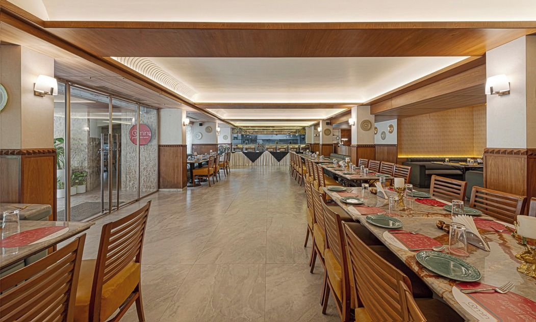 A spacious dining area with multiple tables and chairs, a clear view of the kitchen in the background, and a modern interior design.