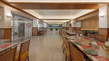 A spacious dining area with multiple tables and chairs, a clear view of the kitchen in the background, and a modern interior design.