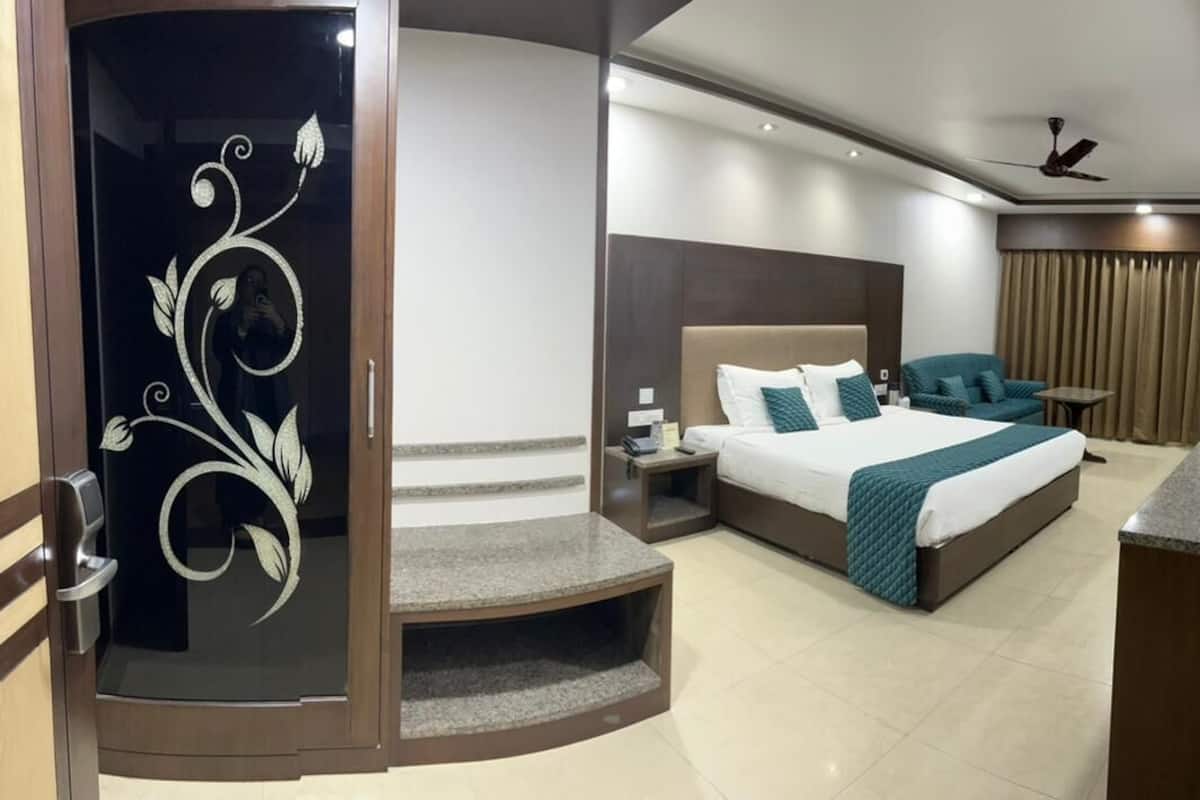 A modern hotel room with a large bed, a desk, a chair, and a small seating area.