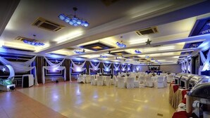 A banquet hall with round tables and white draped curtains. - Hotel Amar (Agra)