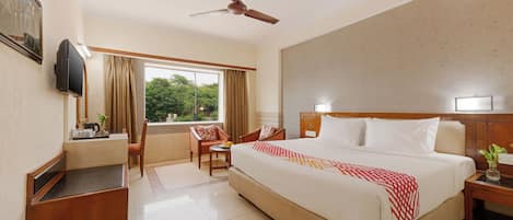 A hotel room with a bed, a desk, a chair, a television, and a window with curtains.