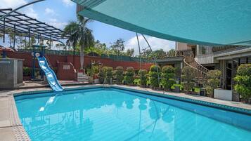 A swimming pool with a slide, a covered area, and a staircase leading to a building.