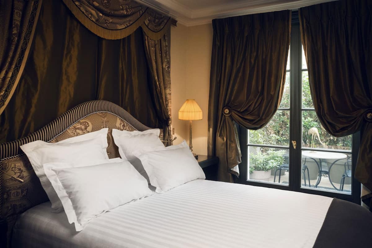 A bed with white linens, a headboard with a lion motif, and a view of greenery through a window.
