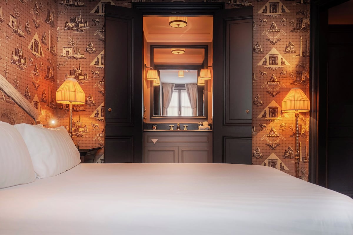 A hotel room with a large bed, two bedside lamps, a mirror, and a view of the city through a window.