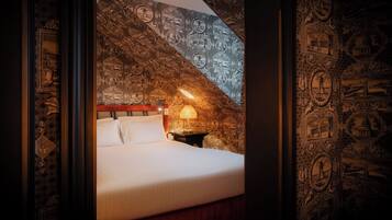 Un dormitorio con cama, mesita de noche y lámpara. Las paredes están decoradas con papel tapiz estampado.