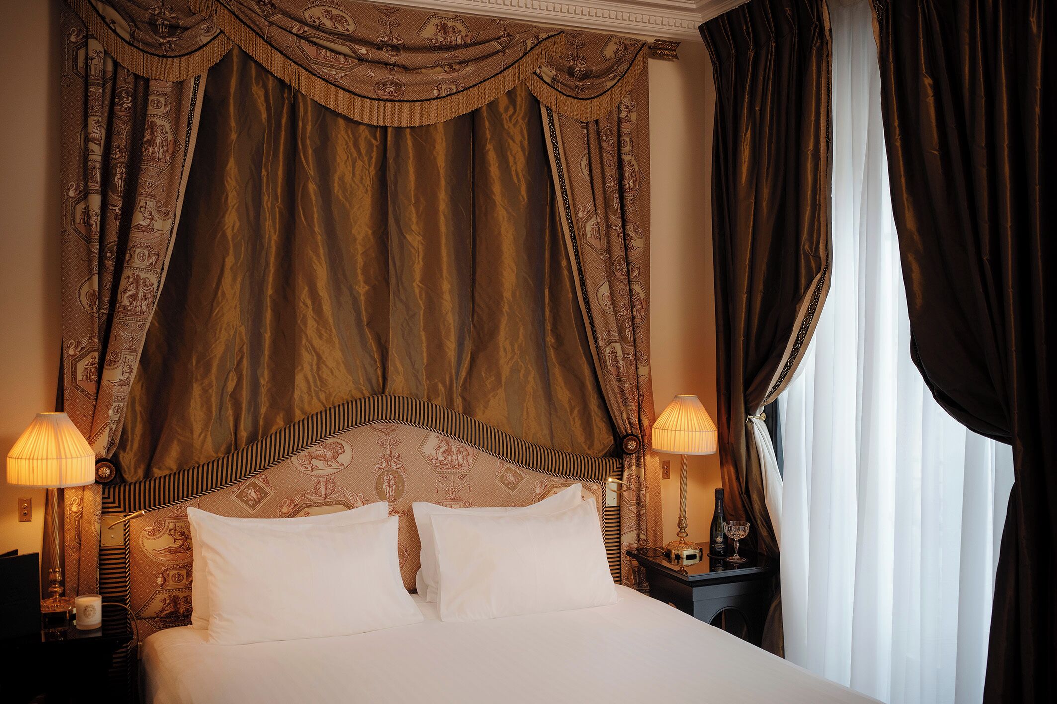 Quarto de hotel com uma cama grande, cabeceira elaborada e duas luminárias de cabeceira.