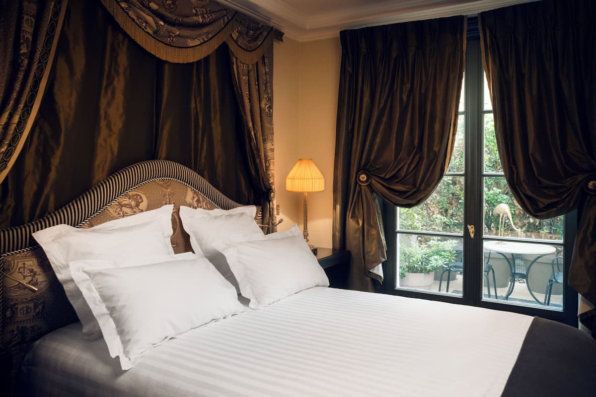 A bedroom with a large bed, dark curtains, and a view of the outdoors through a window.