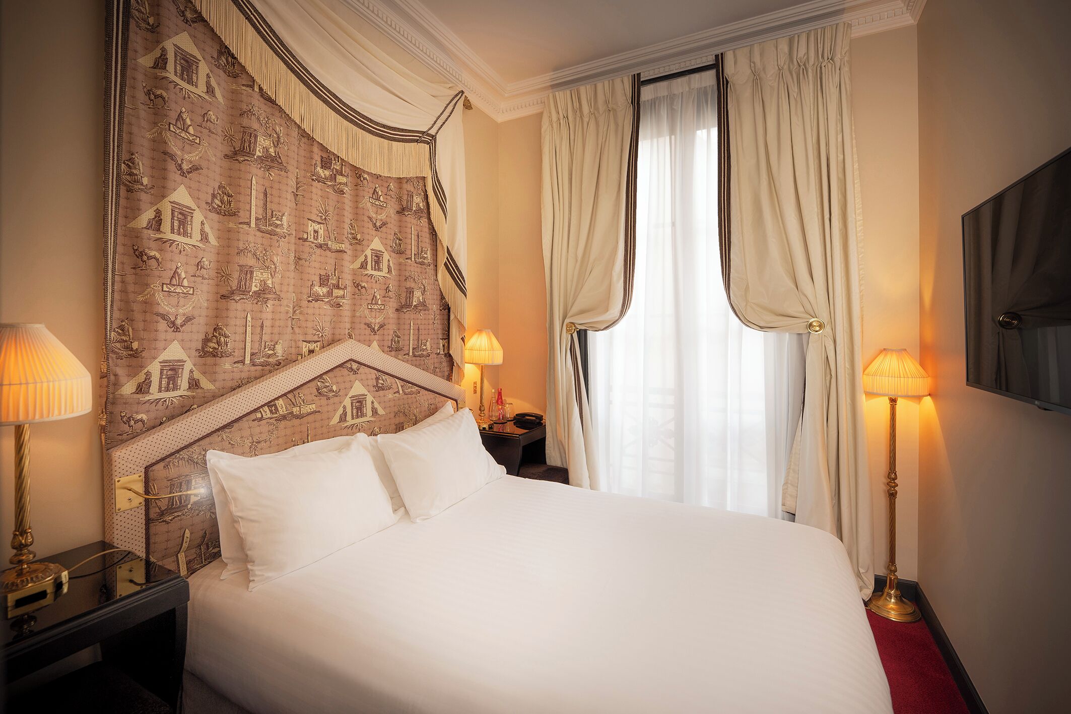 A hotel room with a large bed, two bedside lamps, a nightstand, and a window with curtains.