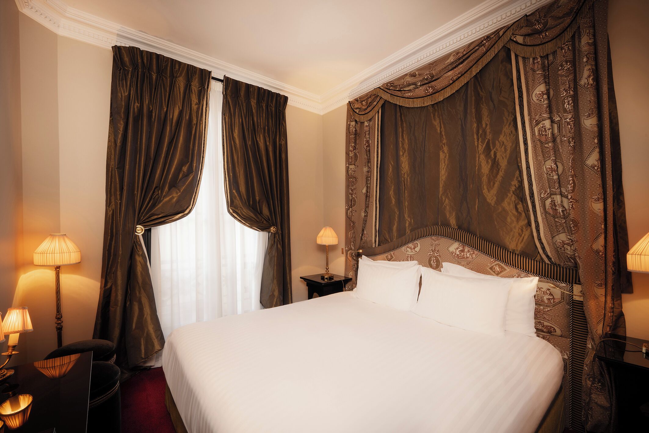 Habitación de hotel con una cama grande, dos lámparas de noche, una mesita de noche y un cabecero con un diseño decorativo.