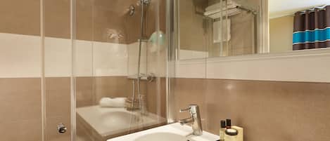 A bathroom with a glass-enclosed shower, a sink with toiletries, and a mirror reflecting the room.