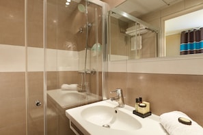 Une salle de bain avec une douche à parois de verre, un lavabo doté d’articles de toilette et un miroir qui reflète la pièce.