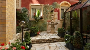A courtyard with a fountain, potted plants, and a glass-enclosed area.