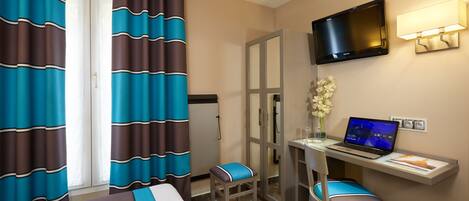 A hotel room with a bed, a desk with a laptop, a TV, and a shower area.