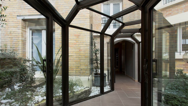 A glass-enclosed corridor with a view of a brick building and a garden with rocks and plants.